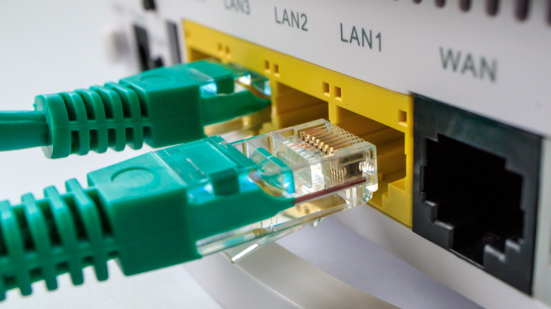 이더넷 포트를 보여주는 라우터의 뒷면. 하나의 녹색 이더넷 케이블이 포트로 슬롯됩니다. 다른 하나는 슬롯이있는 과정에서입니다.
