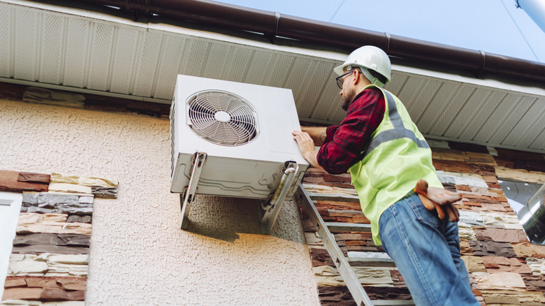 에어컨을 수리하기 위해 사다리에 서있는 균일 한 기술자.