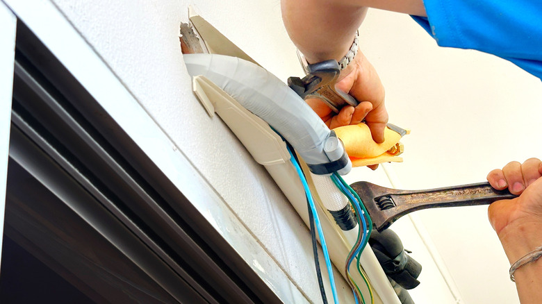 에어컨 드레인 파이프를 설치하고 조립하기 위해 드라이버 또는 도구를 들고있는 에어컨 기술자의 손.