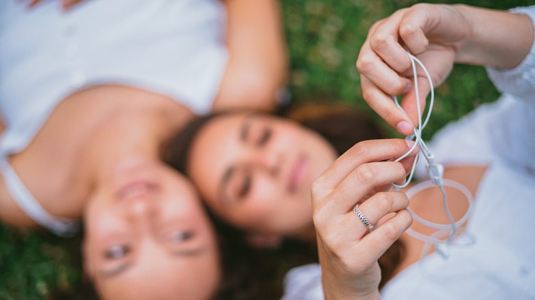 잔디에 누워있는 두 사람, 한 명은 흰색 유선 사과 헤드폰을 카메라 위로 잡고 그들을 풀어주었습니다.
