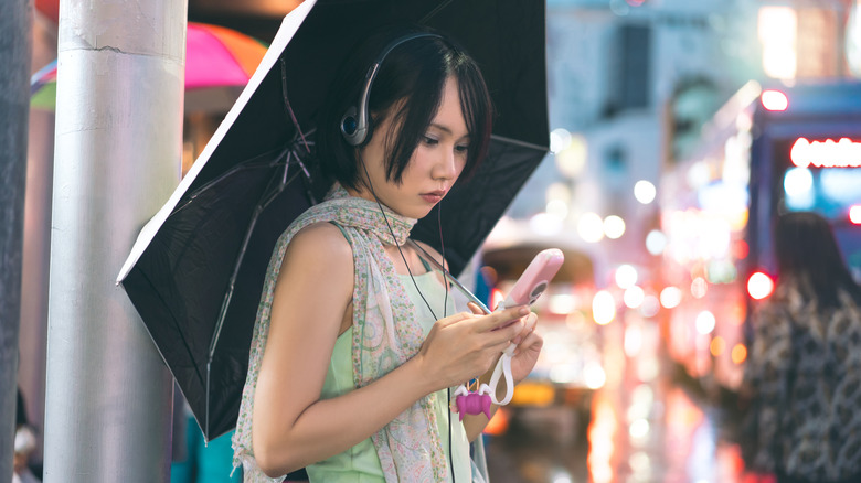 오래된 핑크 플립 폰을 사용하여 y2k 유선 오버 헤드 헤드폰을 착용 한 사람.