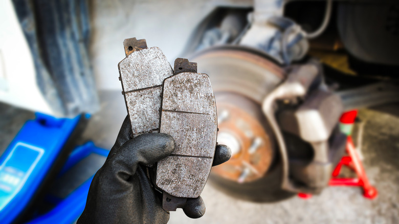 배경에 브레이크 디스크와 캘리퍼가있는 마모 된 브레이크 패드를 들고있는 기술자