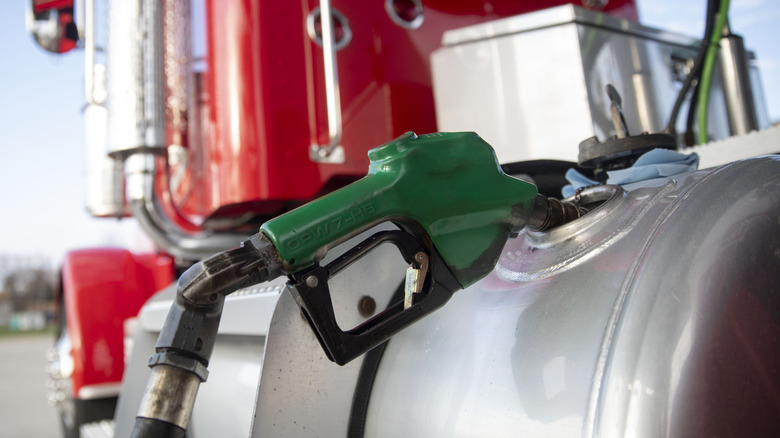 빨간색 반 트럭 트랙터의 연료 탱크에서 무인 녹색 연료 노즐을 닫습니다.