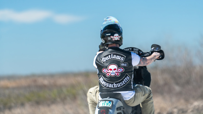 매사추세츠 주 무법자 오토바이 클럽을위한 패치와 함께 검은 가죽 조끼를 착용 한 할리 데이비슨 오토바이를 운전하는 남성