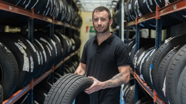 기계공은 타이어로 가득 찬 보관소에 타이어를 잡고 있습니다.