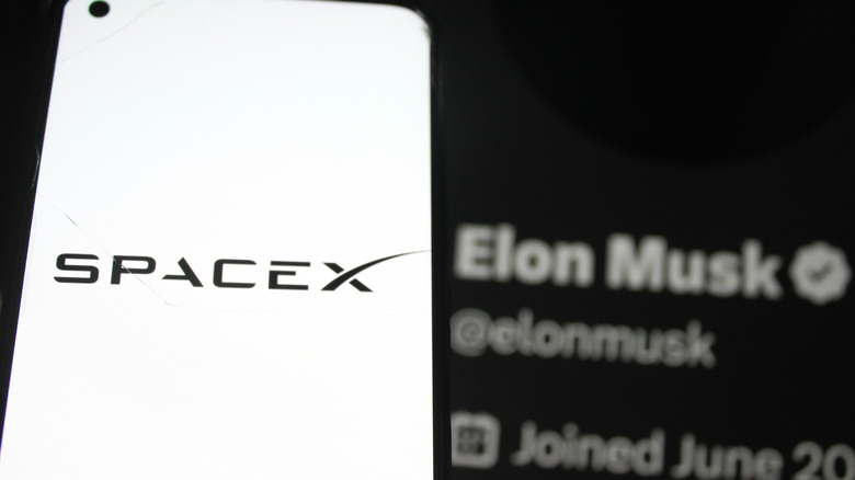 SpaceX 로고는 스마트 폰 화면에 표시됩니다. SpaceX CEO Elon Musk X 프로필 사진으로 백그라운드에 있습니다.
