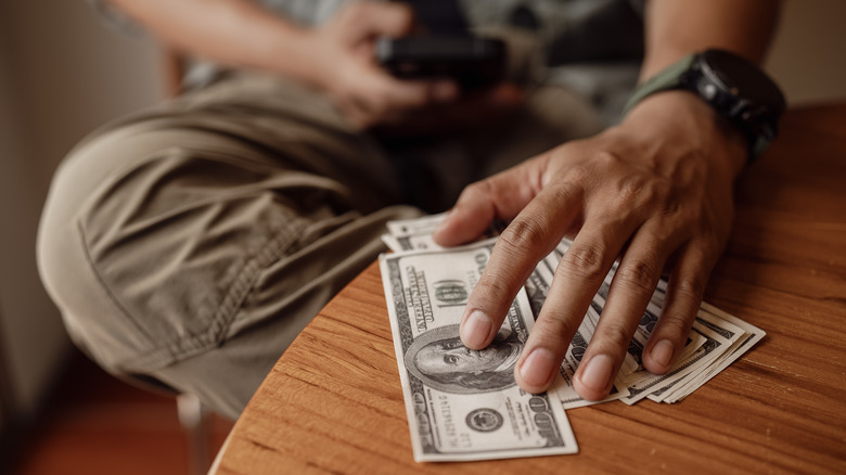 휴대폰에 입력하는 동안 수백 달러를 탁자에 대비하여 수백 달러를 청구하는 사람