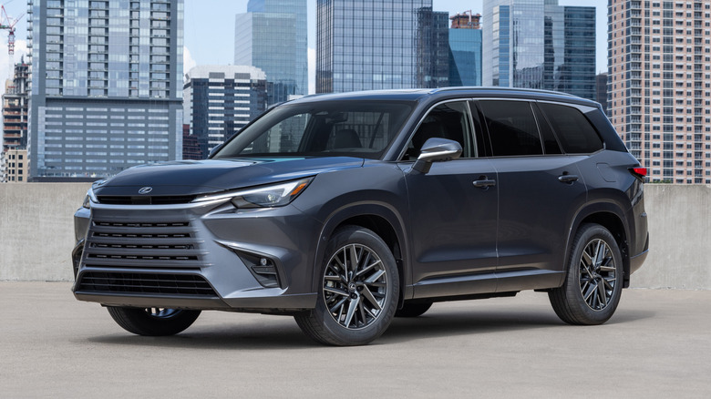 검정색 2026 Lexus TX가 도시 스카이라인을 배경으로 주차되어 있습니다.