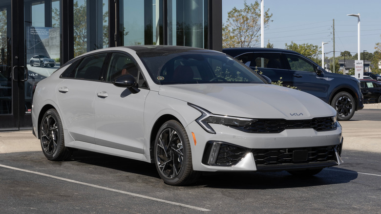 회색 2025 기아 K5의 전면과 측면을 각도로 촬영한 사진입니다.