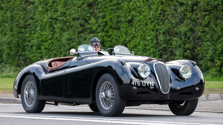 시대에 맞는 레이싱 장비를 장착한 드라이버가 장착된 1954 Jaguar XK120 로드스터