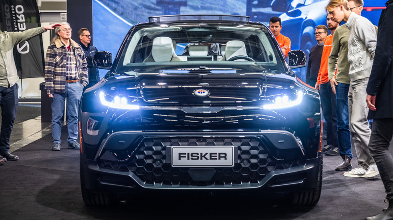 주변 사람들과 함께 전시되어 있는 검은색 Fisker Ocean SUV의 전면 사진입니다.