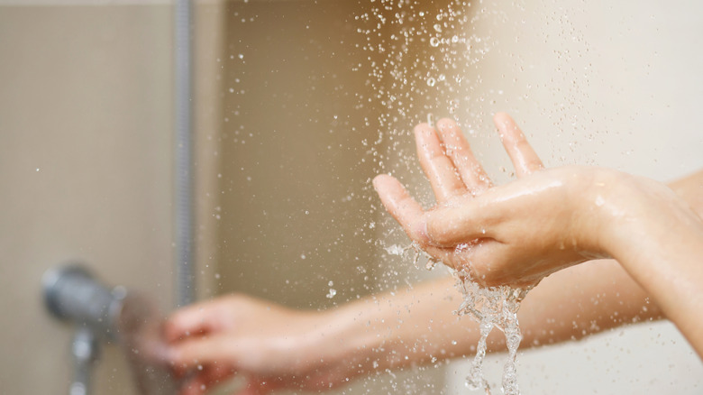 사람이 손을 사용하여 온수기의 물 온도를 측정합니다.