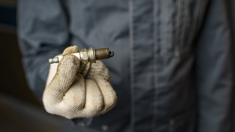 장갑을 낀 정비사가 오염된 점화 플러그를 들고 있습니다.