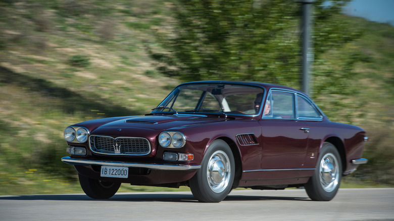부르고뉴색 Maserati 3500 Series One Sebring이 숲이 우거진 시골길을 질주하고 있습니다.