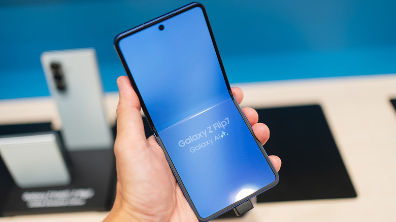 매장 디스플레이 근처에서 Samsung Galaxy Z Flip7 휴대폰을 들고 있는 손 클로즈업