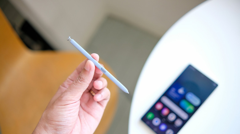 흰색 테이블에 놓인 전화기 위에 스타일러스를 들고 있는 손