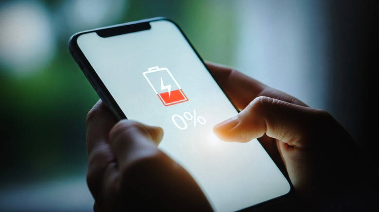 빈 배터리를 보여주는 화면 표시기가 있는 스마트폰을 들고 있는 사람