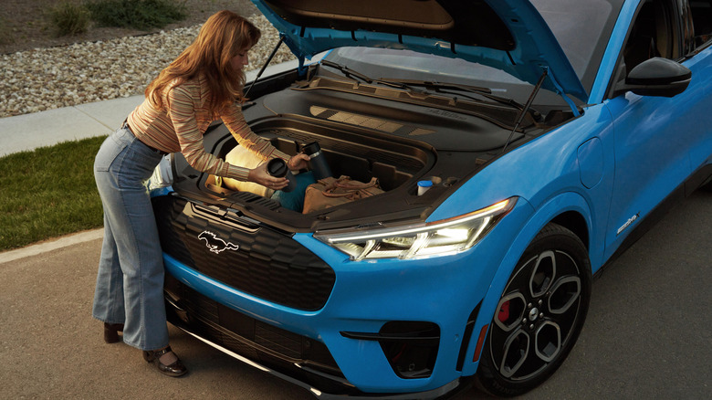파란색 Ford Mustang Mach-E GT의 열린 트렁크에서 물건을 집는 여성