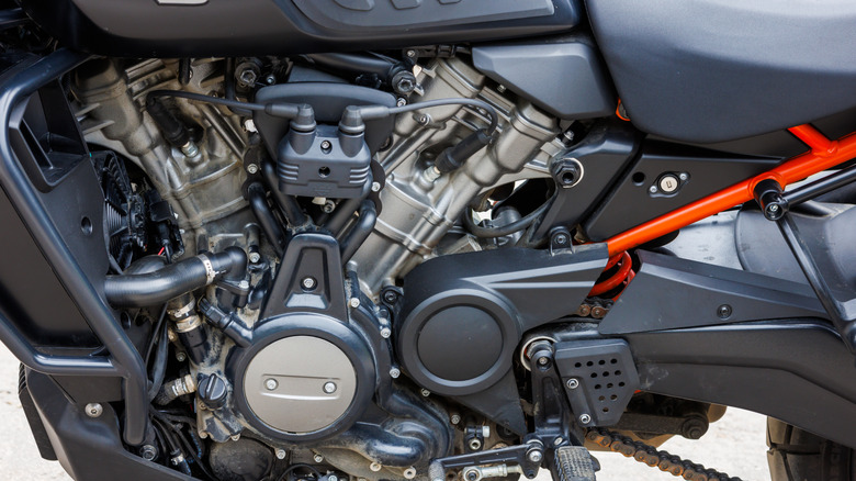 봄날 주차장에 오토바이가 있고, 툴라의 Revolution Max 1250 엔진이 가까이 보입니다.