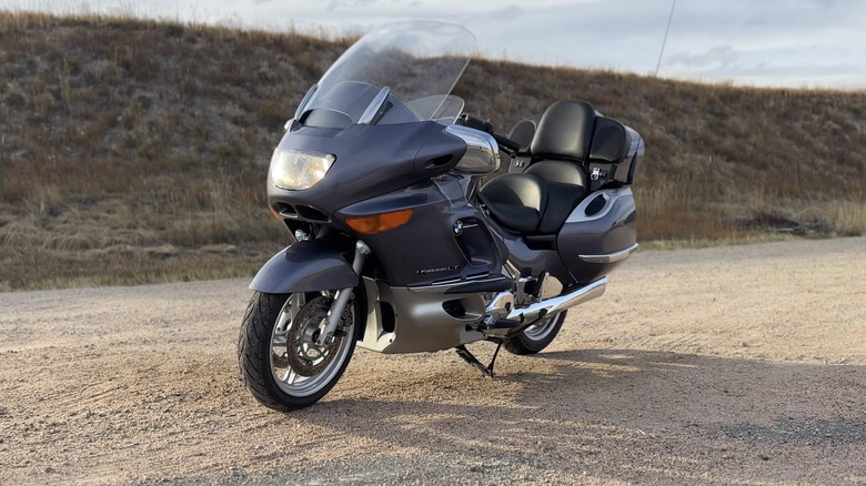 은색 BMW K1200 LT 투어링 크루저 오토바이가 흙 위에 주차되어 오른쪽에서 왼쪽을 향하고 있습니다.