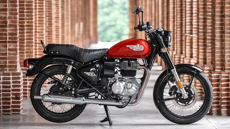 2023년 빨간색 Royal Enfield Bullet 350이 일련의 벽돌 아치 길 옆에 주차되어 있습니다.