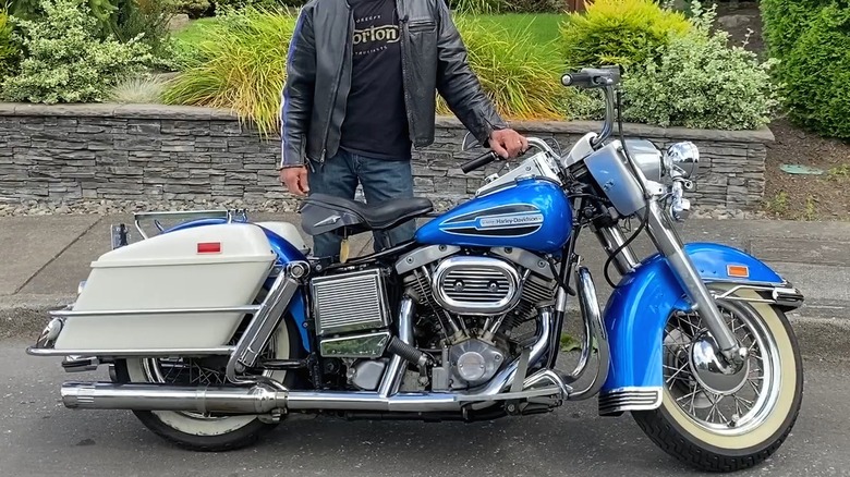 빈티지 블루 1972 Harley Davidson FLH Electra Glide 옆에 가죽 재킷을 입은 사람이 서 있습니다.