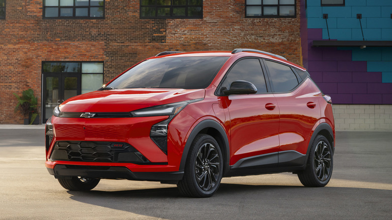 벽돌 건물 앞에 주차된 빨간색 2027 Chevrolet Bolt의 전면 모습