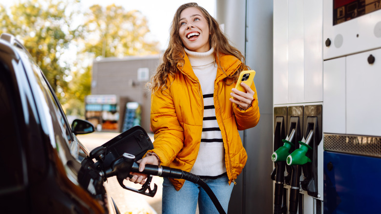 휴대전화를 사용하는 여성이 차에 주유하는 동안 주의를 기울이지 않고 있습니다.
