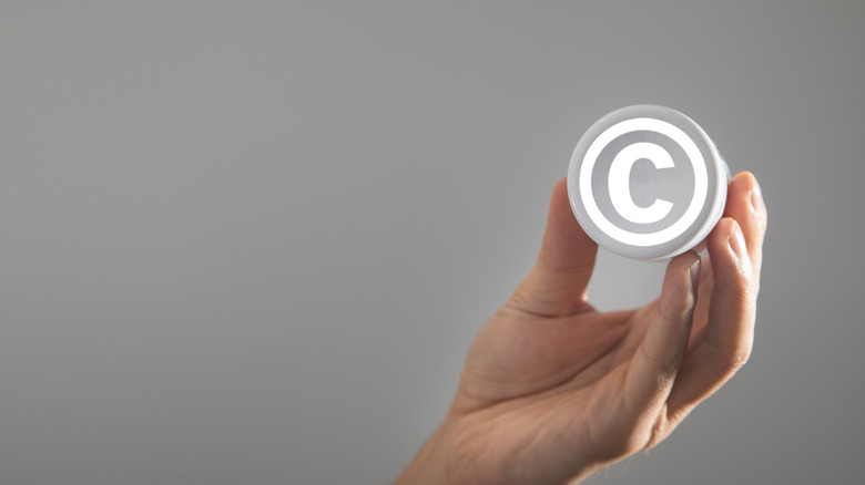 회색 배경 위에 저작권 로고를 들고 있는 손