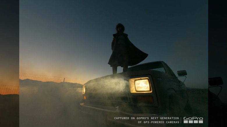 황혼녘에 헤드라이트를 켜고 자동차 후드 위에 서 있는 사람.