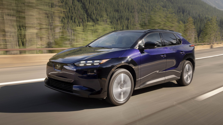 숲속 고속도로에 있는 진한 파란색 Subaru Solterra EV의 전면 3/4 모습.