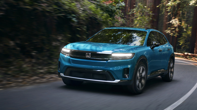 숲길을 주행하는 파란색 혼다 프롤로그 SUV의 전면 모습.