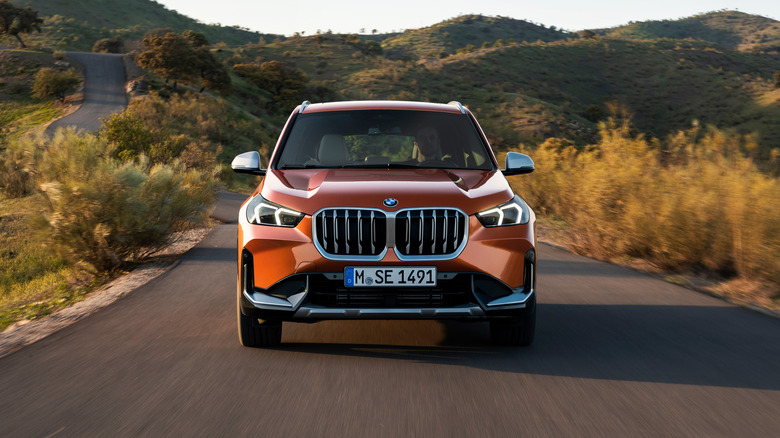 시골 도로를 주행하는 메탈릭 오렌지색 2023 BMW X1의 전면 모습.