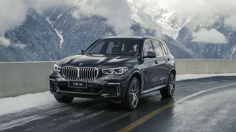 흰 구름과 언덕을 배경으로 눈 덮인 산길을 달리는 2021년형 BMW X5.