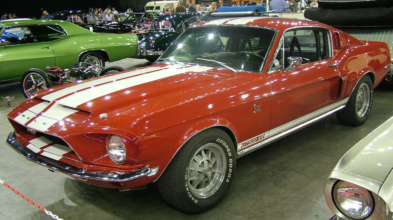 클래식 자동차와 오토바이 사이에 실내에 주차된 1968 Ford Mustang Shelby GT500 KR, 전면 왼쪽 3/4 뷰