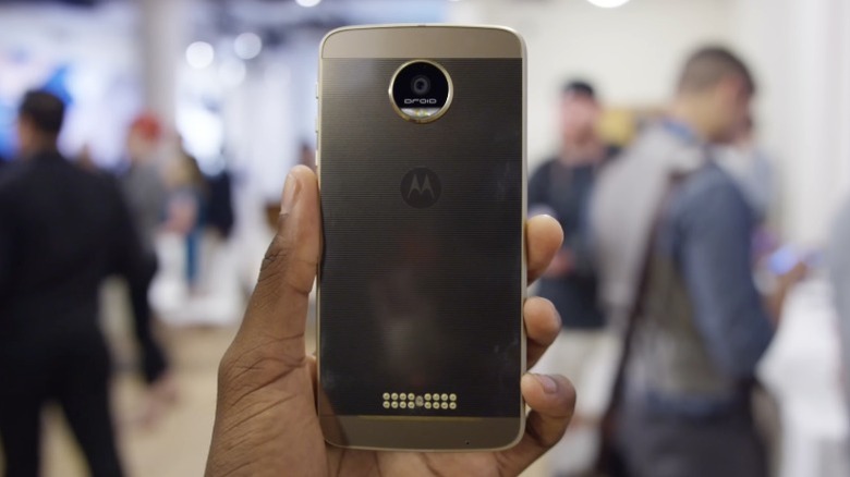 초점이 맞지 않는 사람들을 배경으로 Moto Z를 들고 있는 손