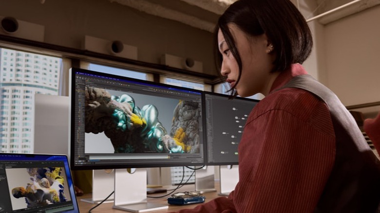 Apple Studio Display 옆에서 노트북을 보고 있는 여성