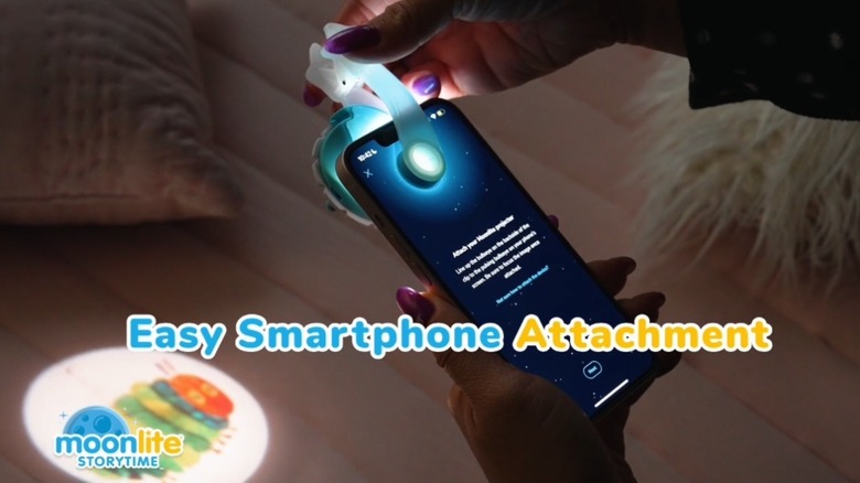한 여성이 iPhone에 Moonlight Storytime Projector를 연결하고 있습니다.