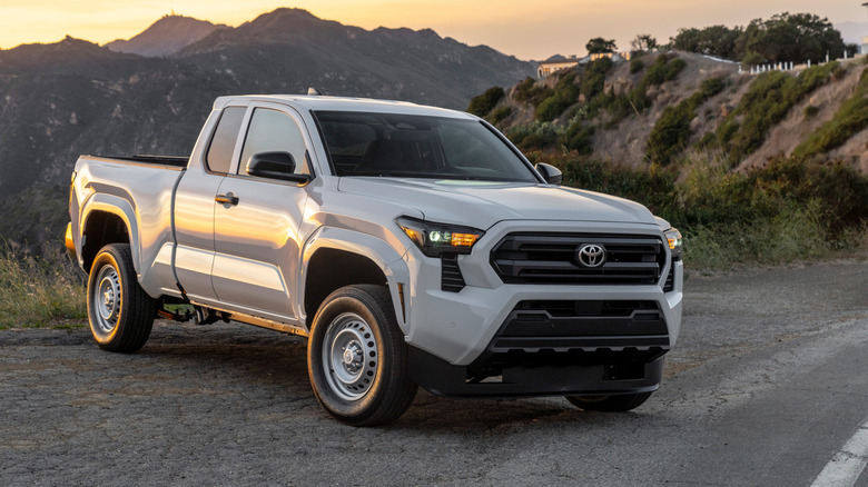 산악 도로에 주차된 흰색 2026 Toyota Tacoma SR의 전면 3/4 뷰.