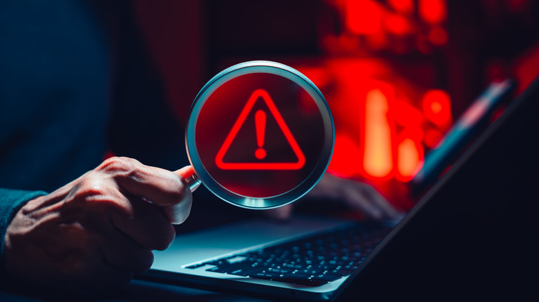 노트북 위에 디지털 경고 기호가 있는 돋보기를 들고 있는 사람