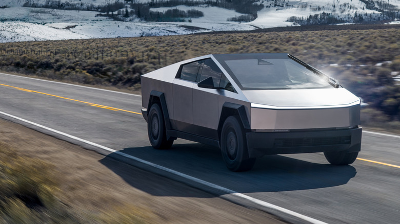 눈이 내리는 시골 고속도로를 주행하는 Tesla Cybertruck의 전면 3/4 모습.