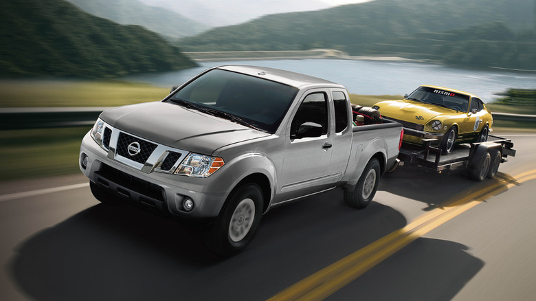 트레일러에서 노란색 Datsun 240Z를 견인하는 은색 Nissan Frontier 픽업 트럭.