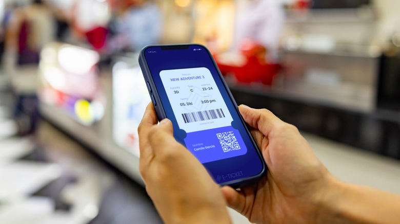 영화관 매점 근처 누군가의 손에 스마트폰에 표시된 영화 티켓의 클로즈업