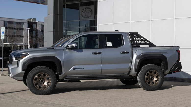 Toyota 대리점 앞에 주차된 은색 Toyota Tacoma Trailhunter의 측면 모습.