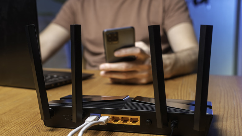 테이블 위에 놓인 검정색 Wi-Fi 라우터와 노트북과 스마트폰을 사용하는 남자