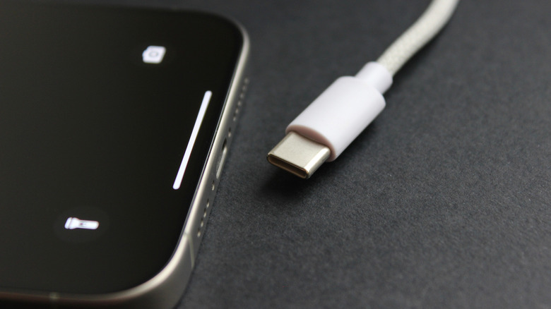 어두운 표면에 있는 최신 스마트폰 옆에 있는 USB-C 케이블 클로즈업