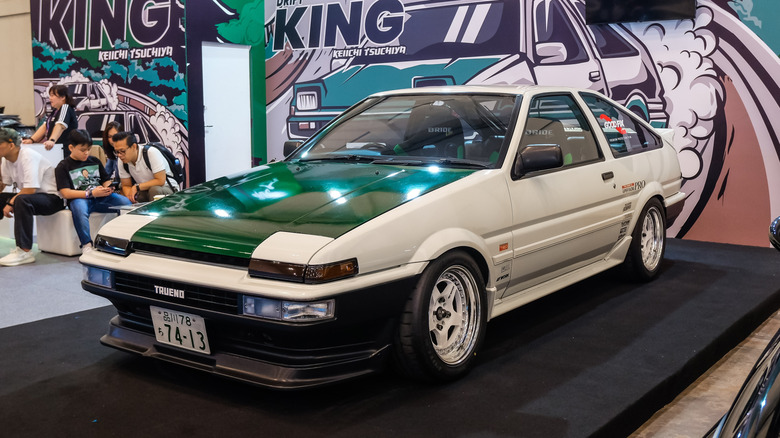 자동차 쇼에 전시된 흰색 AE86 Toyota Corolla의 전면 3/4 뷰.