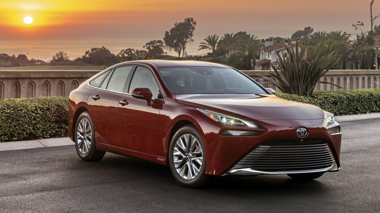 일몰 시 교외 거리에 주차된 빨간색 2023 Toyota Mirai의 전면 3/4 전망.