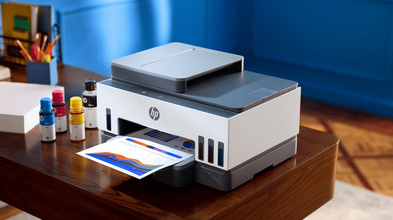 잉크병 옆 테이블 위에 놓인 HP 스마트 탱크 7000 프린터.