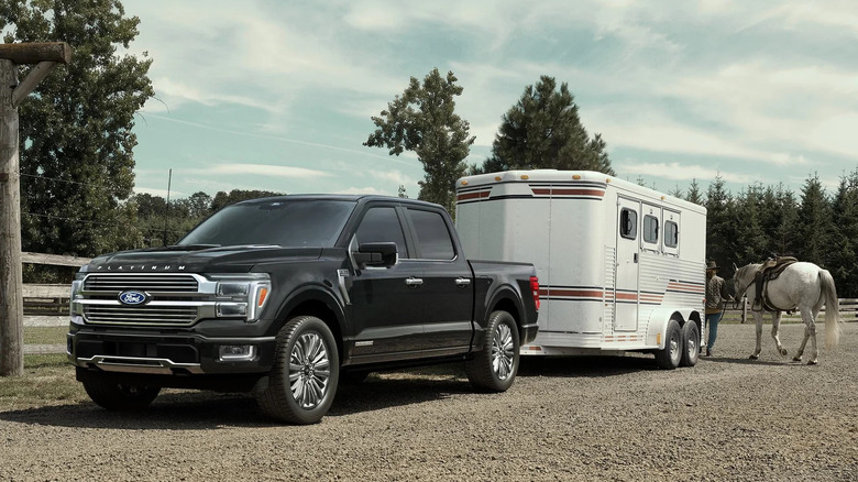 목장에 있는 검정색 Ford F-150 하이브리드 견인 말 트레일러의 전면 3/4 전망.